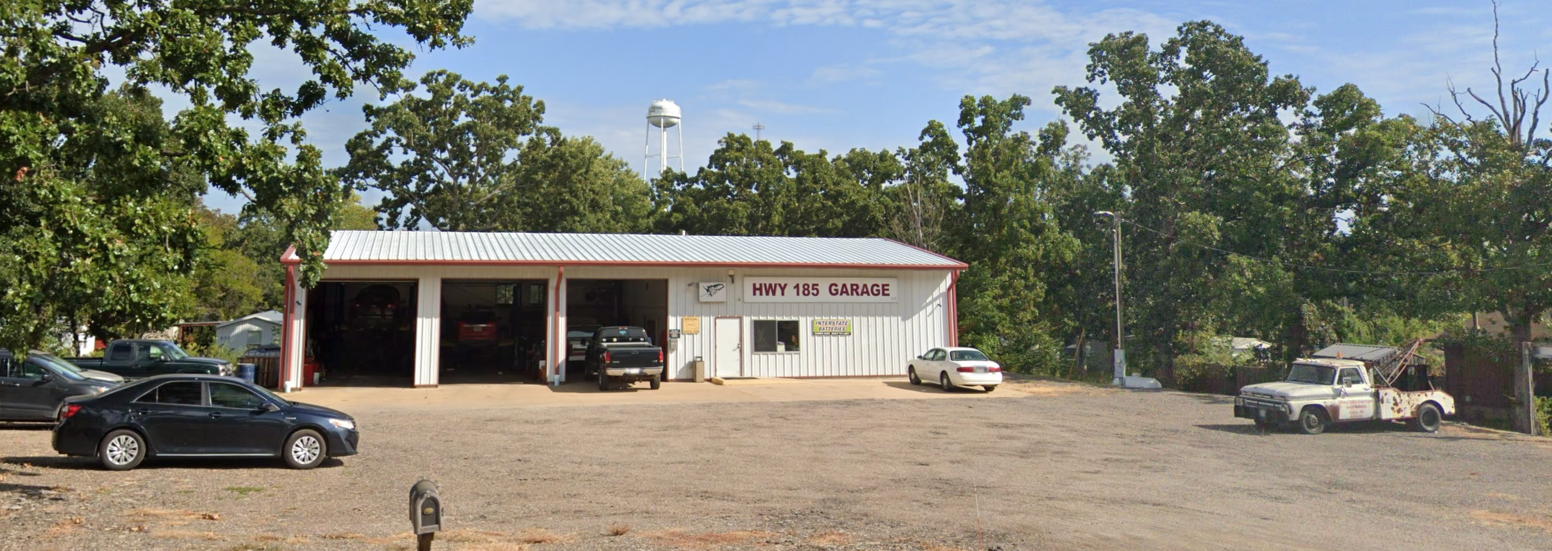 Wide view of Highway 185 Garage and its driveway, surrounded by trees
